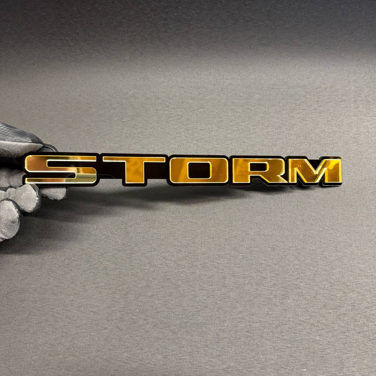STORM custom text car badge in gold and black, automotive emblem for Ford, Chevrolet, Dodge, RAM, GMC and Jeep vehicles.