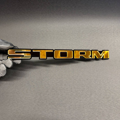 STORM custom text car badge in gold and black, automotive emblem for Ford, Chevrolet, Dodge, RAM, GMC and Jeep vehicles.