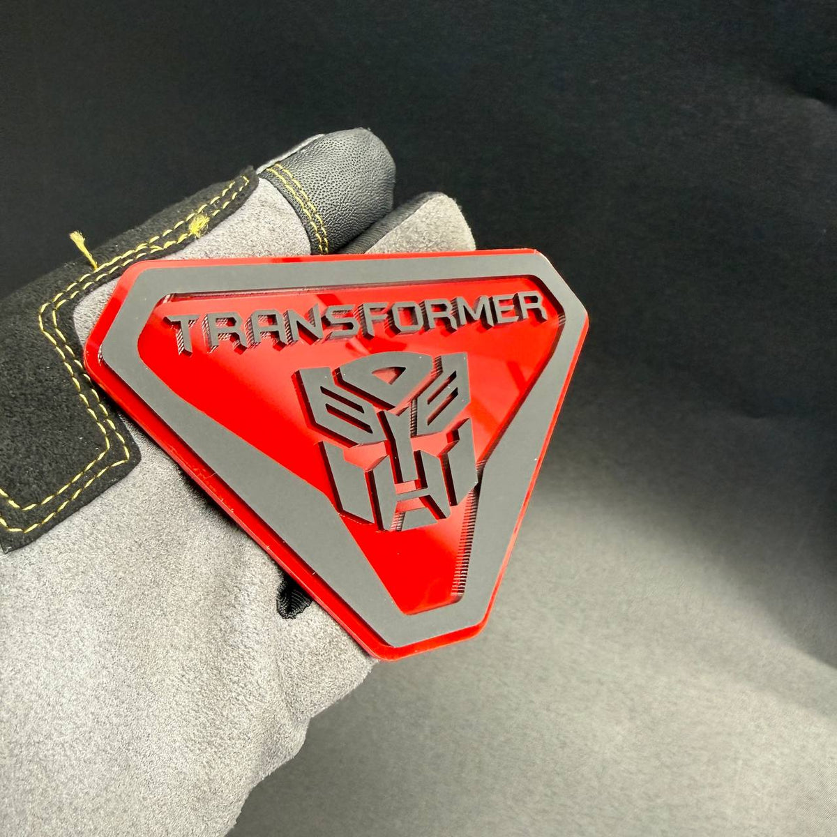Red and silver Transformer Autobot automotive badge with detailed robot face logo and angular shield border.