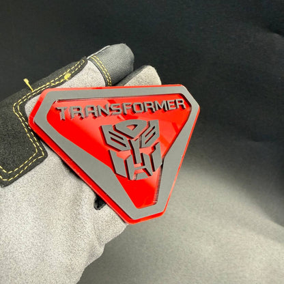 Red and silver Transformer Autobot automotive badge with detailed robot face logo and angular shield border.