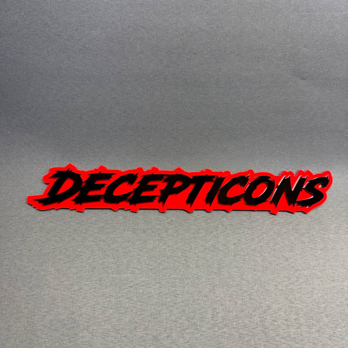 Transformers-inspired Decepticon text tailgate emblem featuring black raised lettering on bright red acrylic, Toyota Tacoma truck styling accessory.