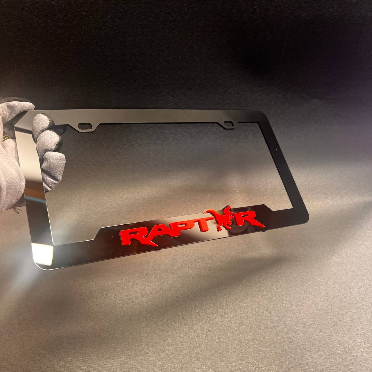 Custom car plate frame with black finish and red Raptor emblem accent