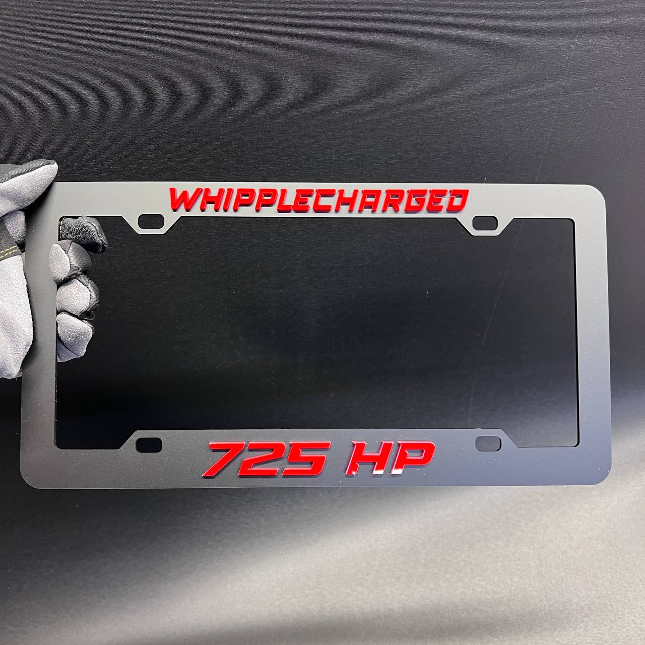 Whipplecharged 725 HP car license plate frame with red raised lettering and black finish.