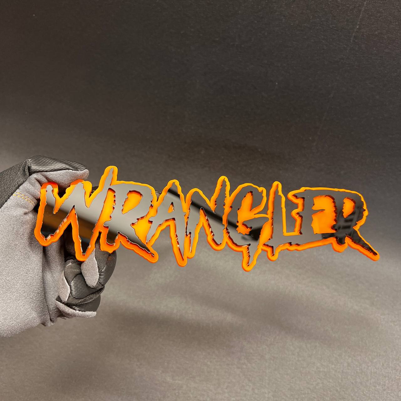 3D Wrangler text emblem with orange acrylic outline and black face.