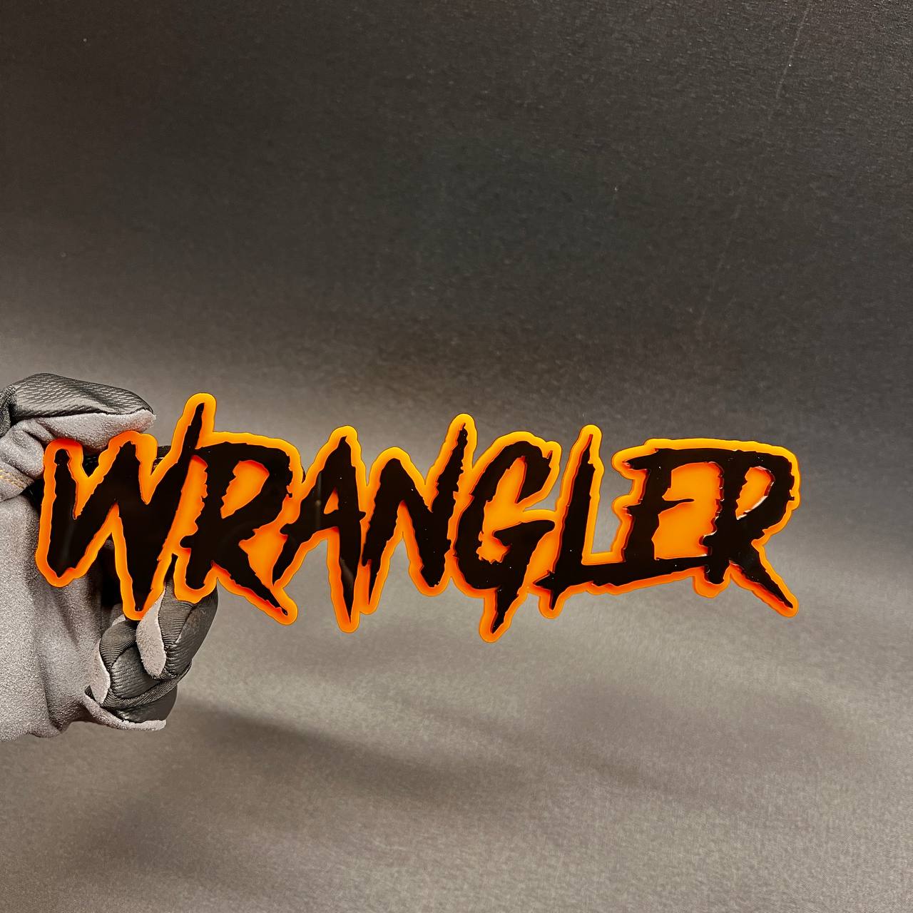 Wrangler custom text car badge in black with orange outline for vehicle exterior.