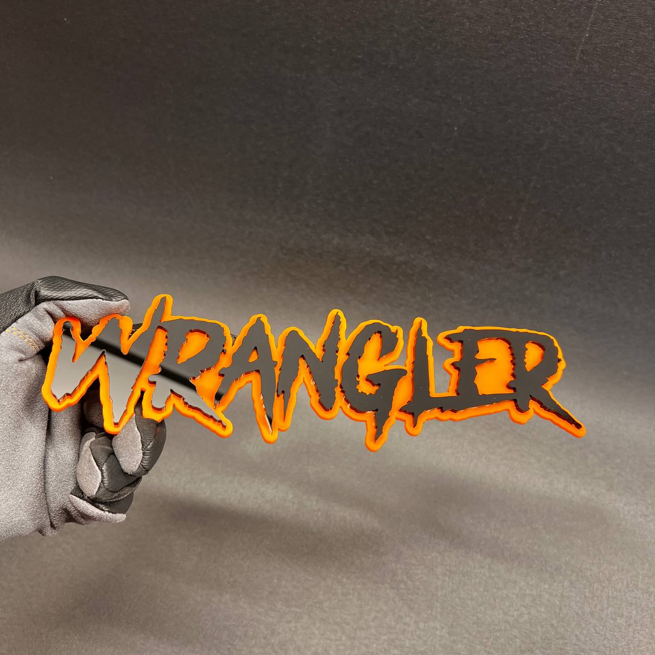 Black and orange Wrangler exterior emblem for grille, tailgate, or body panel.