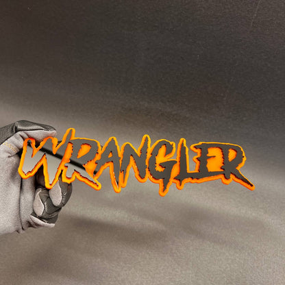 Black and orange Wrangler exterior emblem for grille, tailgate, or body panel.